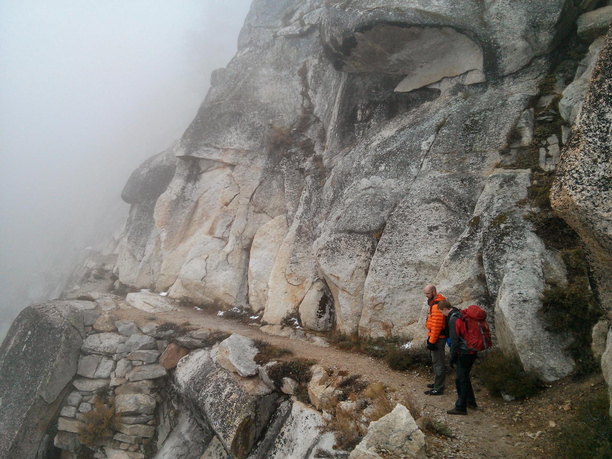 Two hikers on a narrow mountain path in the fog.